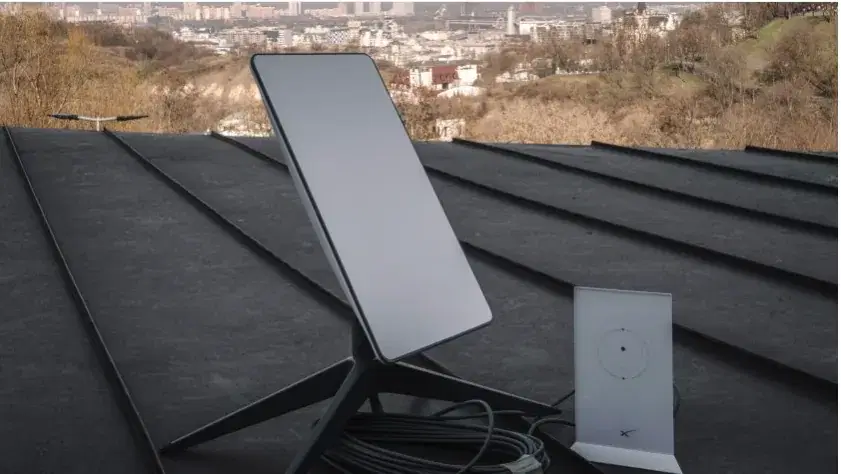 Starlink dish and router on a dark metal roof, with a city beyond the hill.